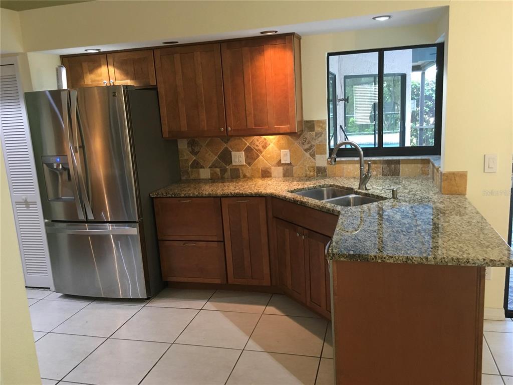 A kitchen features wood cabinets, granite countertops, stainless steel appliances, and a tiled backsplash — 1703 PADDOCK DRIVE, PLANT CITY, FL