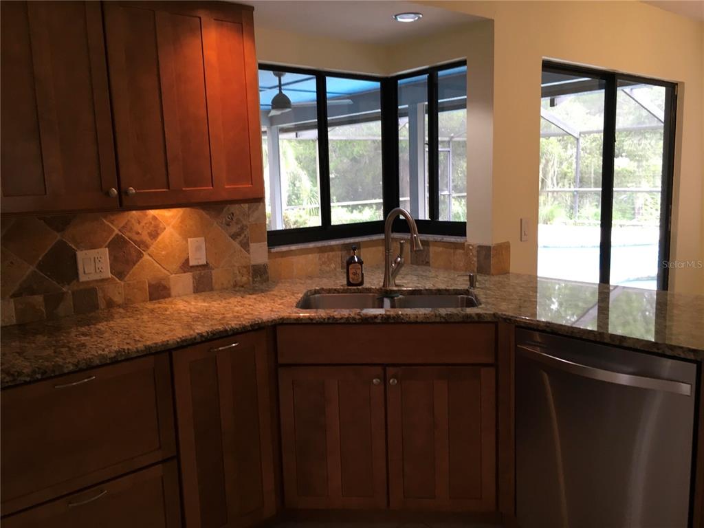 A kitchen features wood cabinets, granite countertops, a corner sink, and a view of a pool — 1703 PADDOCK DRIVE, PLANT CITY, FL