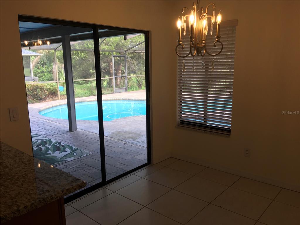 A dining area with tile floors and a chandelier overlooks a patio and swimming pool — 1703 PADDOCK DRIVE, PLANT CITY, FL