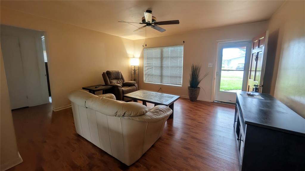 A living room features a beige sofa, a recliner, a coffee table, and wood-look flooring — 969 6TH AVENUE NE, LARGO, FL