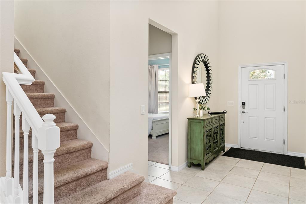 An entryway features a carpeted staircase, a green cabinet, a round mirror, and a front door — 1599 LIMA AVENUE, KISSIMMEE, FL