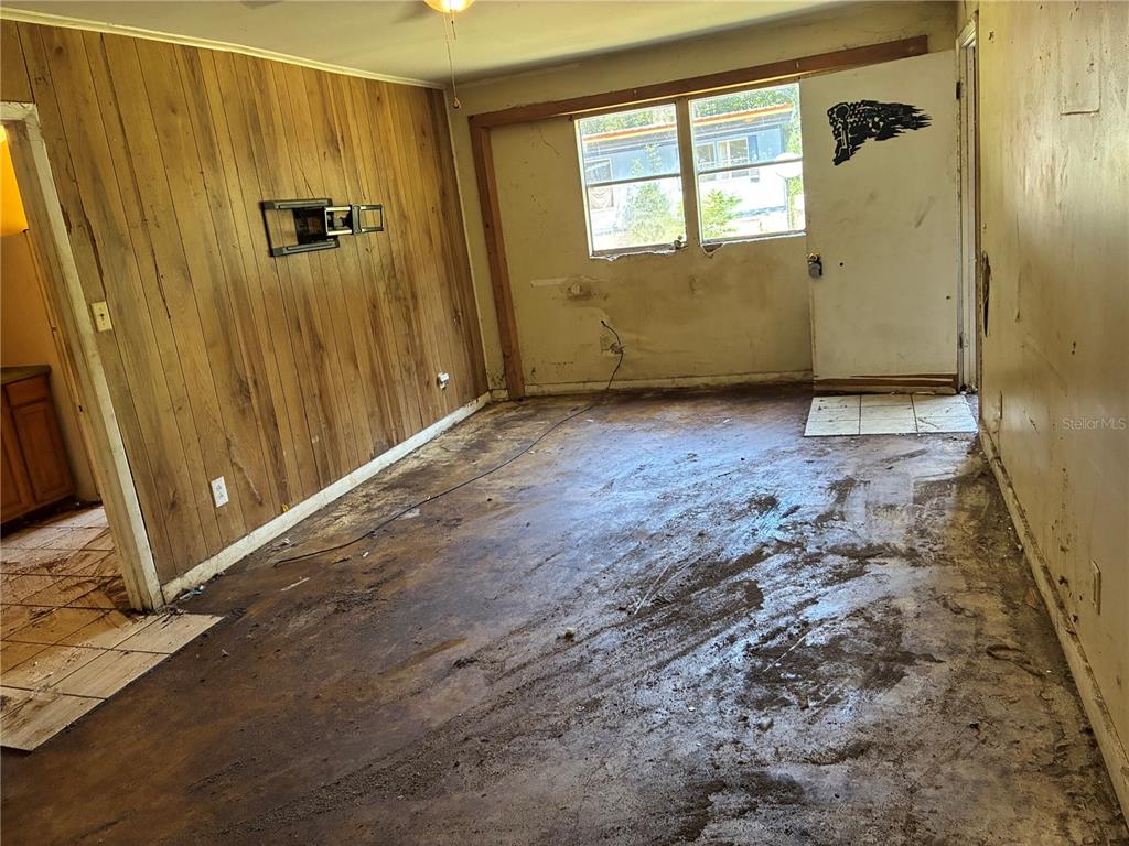 A room with wood-paneled walls, a window, and a floor covered in dirt and debris — 17990 SE 51ST STREET, OCKLAWAHA, FL