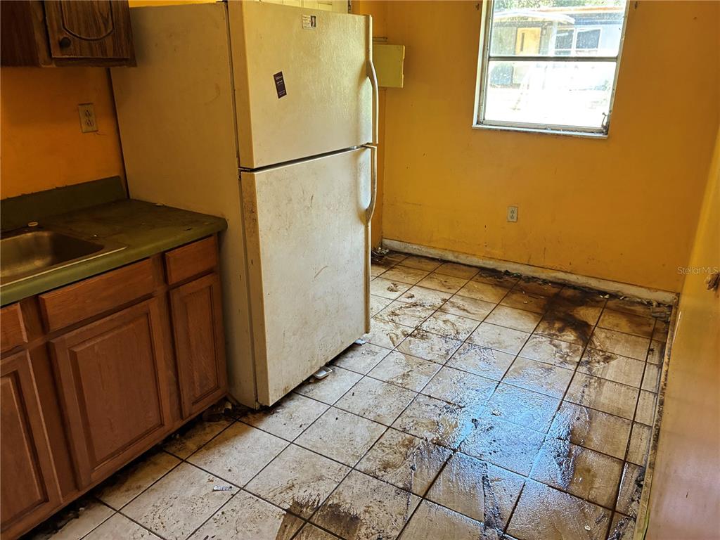 A kitchen with yellow walls, a white refrigerator, wood cabinets, and dirty tiled flooring — 17990 SE 51ST STREET, OCKLAWAHA, FL