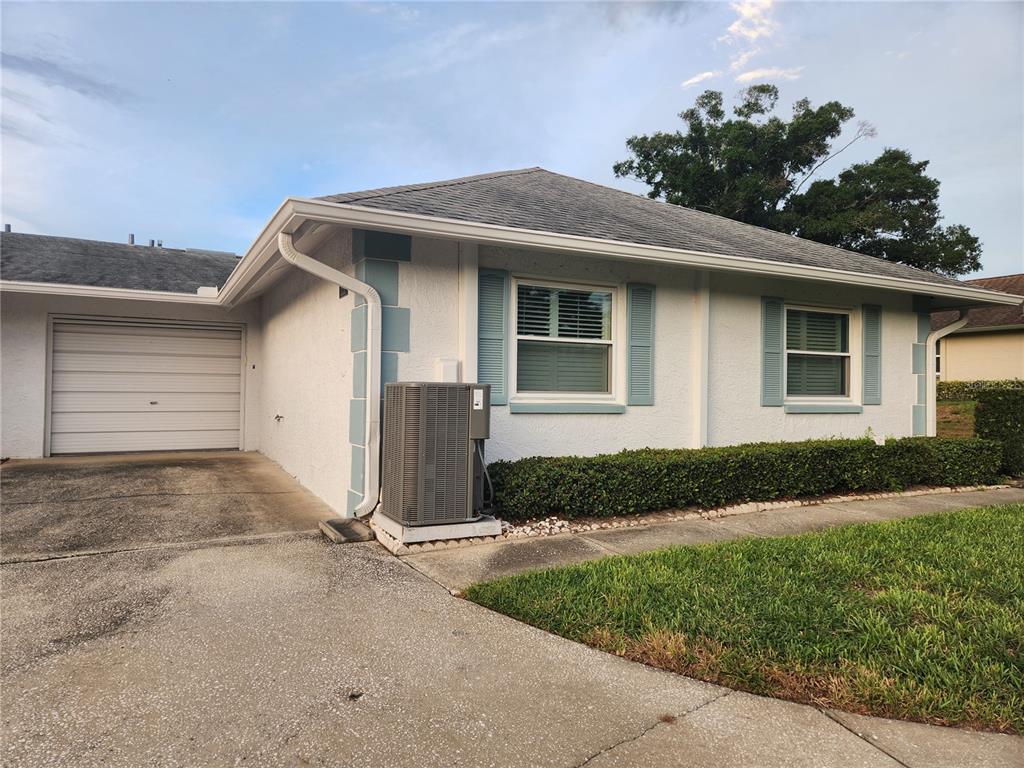 A single-story house exterior features a garage, light-colored stucco walls, blue shutters, and an AC unit — 1251 SUTHERLAND COURT, DUNEDIN, FL