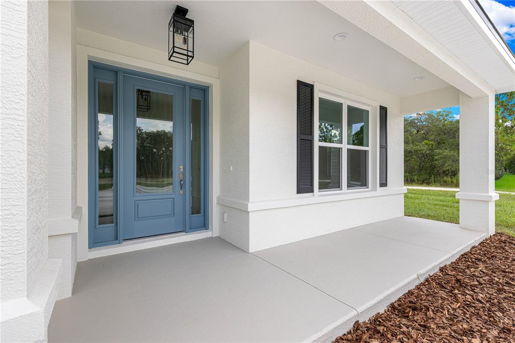 A blue front door with sidelights sits on a covered porch with white stucco walls — 12359 SW 88 STREET, DUNNELLON, FL