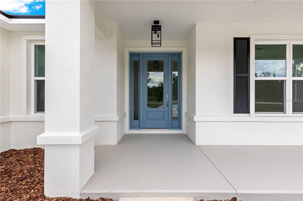 A covered front porch features a blue door with sidelights and white stucco walls — 12359 SW 88 STREET, DUNNELLON, FL