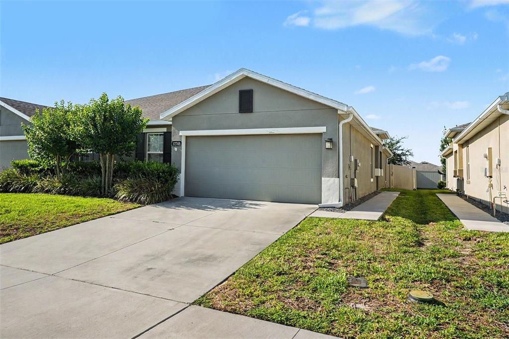 A single-story house exterior features a gray garage door, a concrete driveway, and green landscaping — 17745 TURNING LEAF CIRCLE, LAND O LAKES, FL
