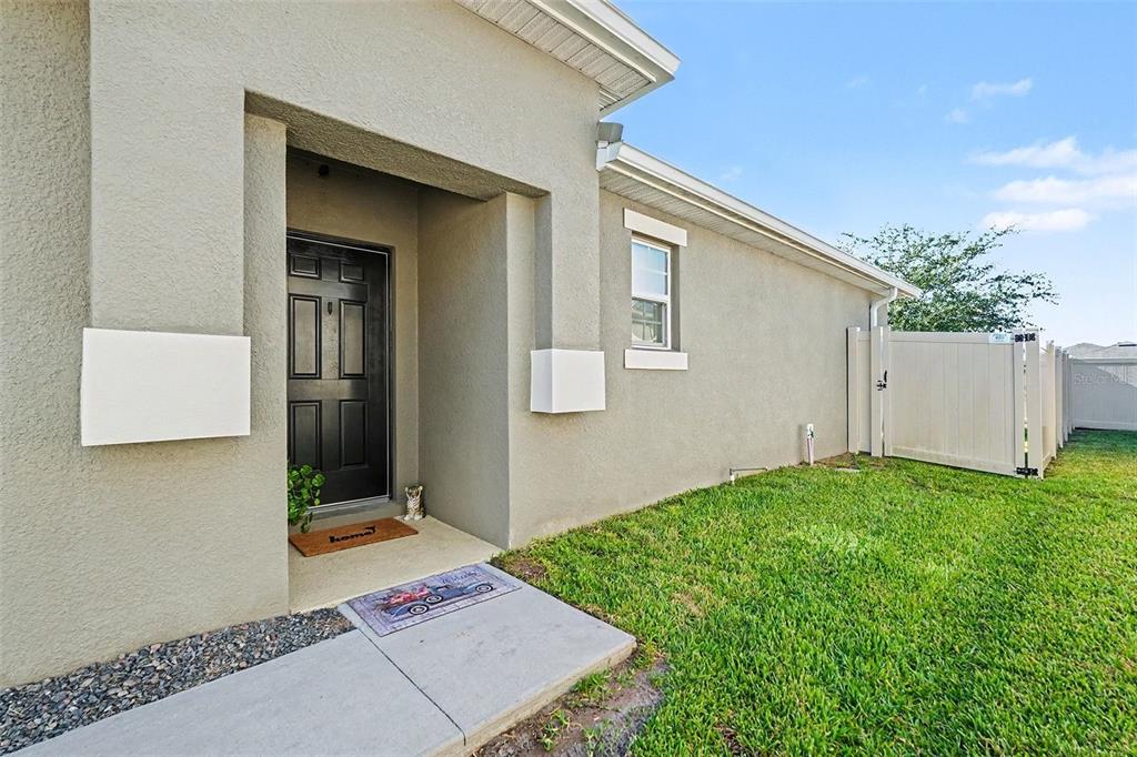 A beige stucco house exterior features a black front door and a white vinyl fence — 17745 TURNING LEAF CIRCLE, LAND O LAKES, FL