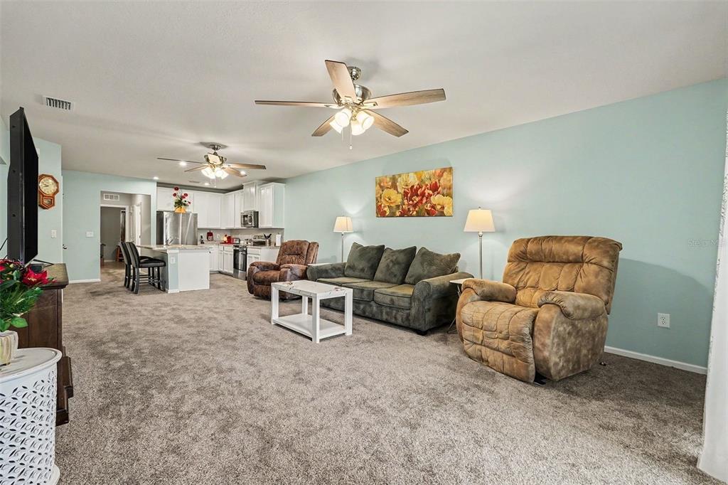 A living room with gray carpet, a green sofa, two recliners, and an open kitchen — 17745 TURNING LEAF CIRCLE, LAND O LAKES, FL