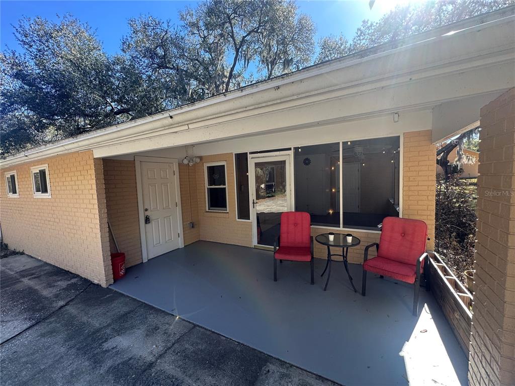 A covered brick patio features a white door, a glass-paneled door, and two red chairs — 5520 OHIO AVENUE, LADY LAKE, FL