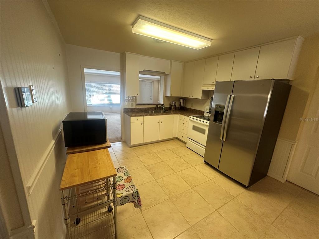 A kitchen features white cabinets, stainless steel appliances, tile flooring, and a wooden rolling cart — 5520 OHIO AVENUE, LADY LAKE, FL