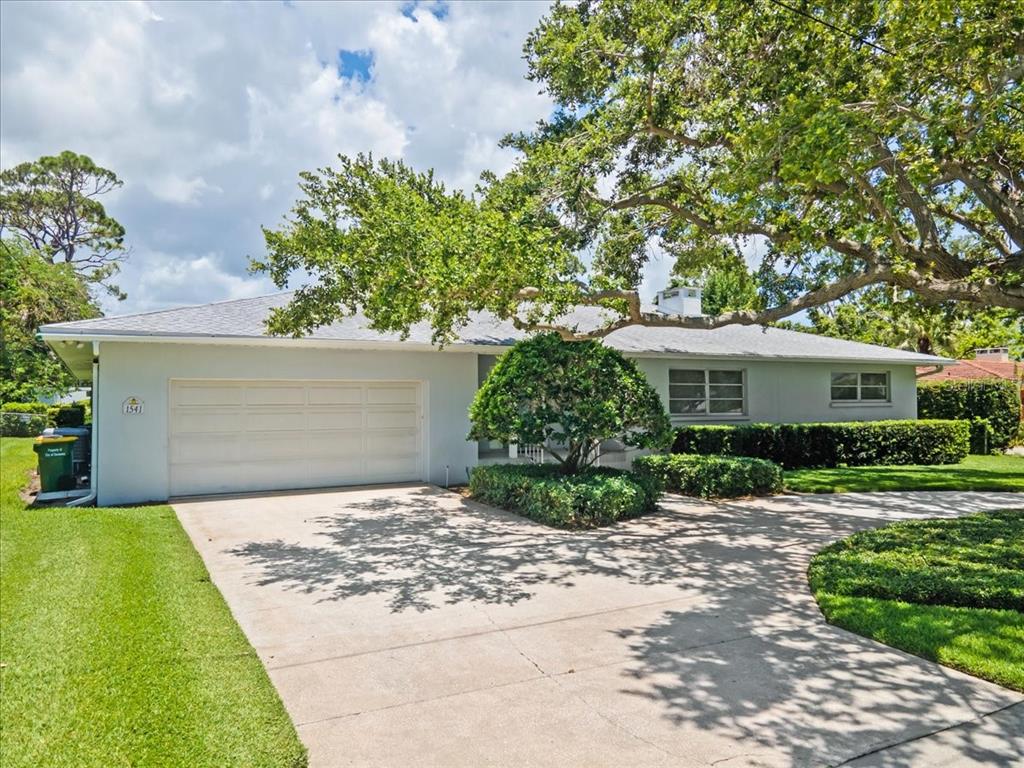 A single-story house with a white garage, concrete driveway, and a large tree in front — 1541 FLOWER DRIVE, SARASOTA, FL