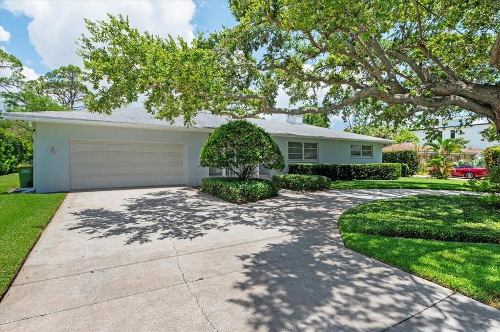 A single-story house with a white garage, a concrete driveway, and a large shade tree — 1541 FLOWER DRIVE, SARASOTA, FL