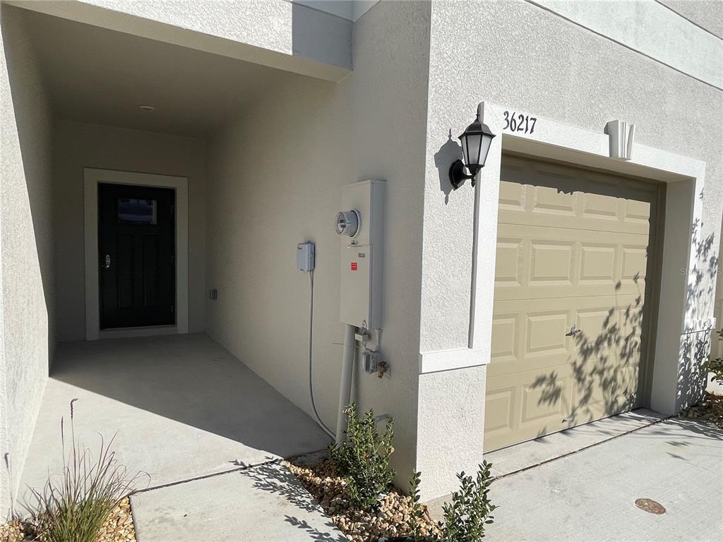 A tan garage door and a recessed front entrance are visible on this stucco home — 36217 RISA MICHELE STREET, ZEPHYRHILLS, FL