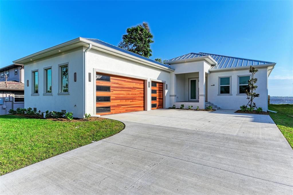 A modern white house with a metal roof and wood-paneled garage doors — 112 NORTHSHORE TERRACE, PORT CHARLOTTE, FL