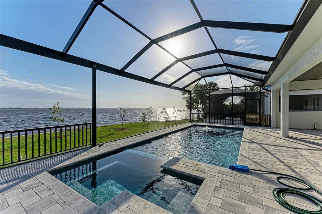A screened-in pool and spa overlook a large body of water from a paved patio — 112 NORTHSHORE TERRACE, PORT CHARLOTTE, FL