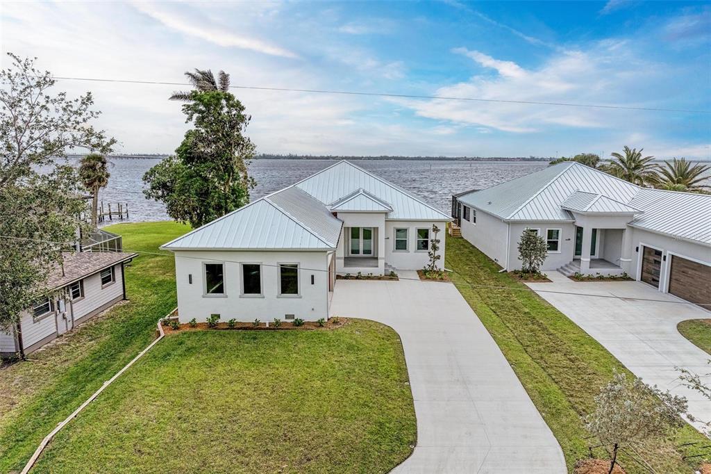 An aerial view shows two modern white houses with metal roofs beside a large body of water — 112 NORTHSHORE TERRACE, PORT CHARLOTTE, FL