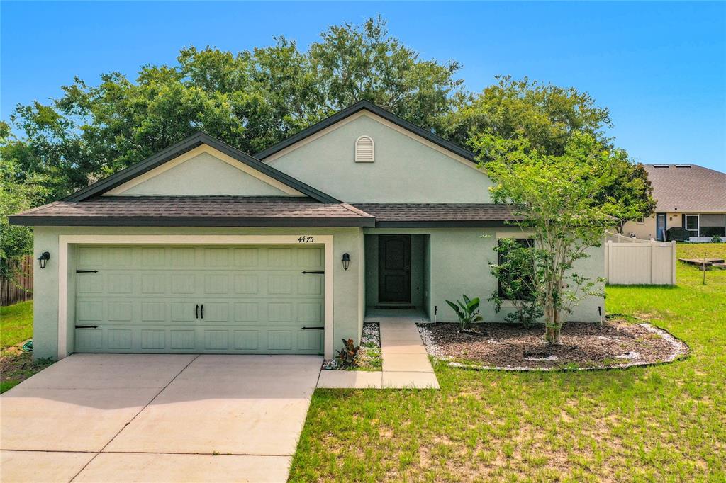 A single-story house with a green garage door, stucco exterior, and a front walkway — 4475 CAICOS DRIVE, TAVARES, FL
