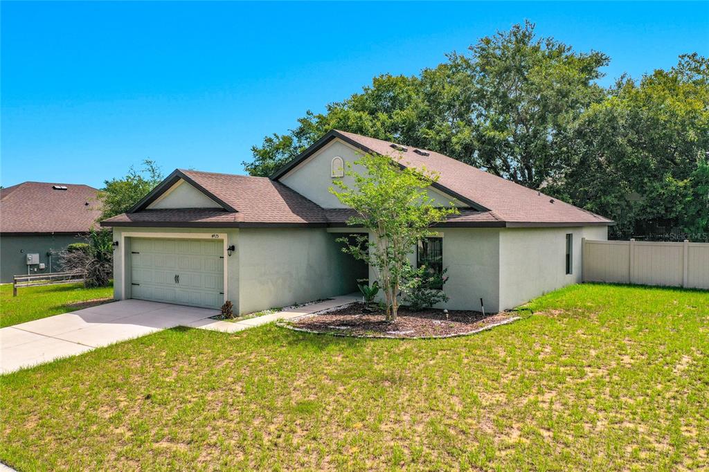 A single-story house with a two-car garage, light-colored stucco exterior, and a brown shingled roof — 4475 CAICOS DRIVE, TAVARES, FL
