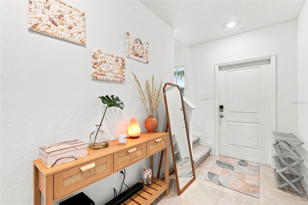 An entryway features a wooden console table, a floor mirror, and seashell wall art — 13969 LILAC SKY TERRACE, BRADENTON, FL