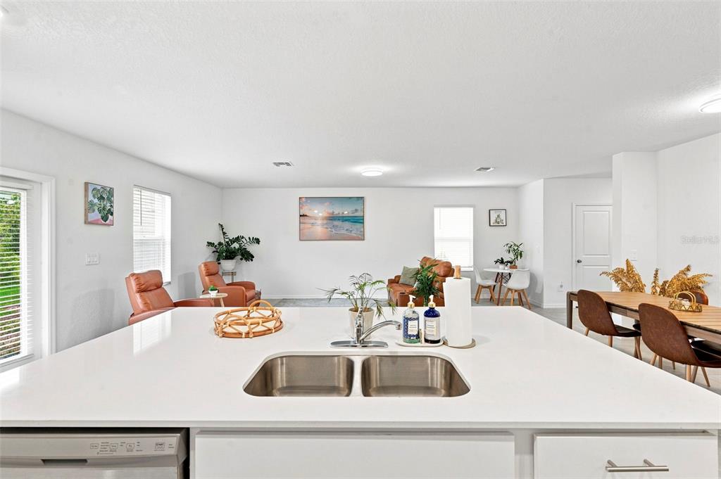 A kitchen island with a double sink overlooks an open-concept living and dining area — 13969 LILAC SKY TERRACE, BRADENTON, FL