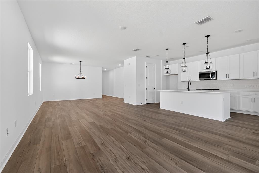 An open-concept kitchen and living area with white cabinets, a kitchen island, and wood-look flooring — 30130 EMERALD FOREST DRIVE, MOUNT DORA, FL