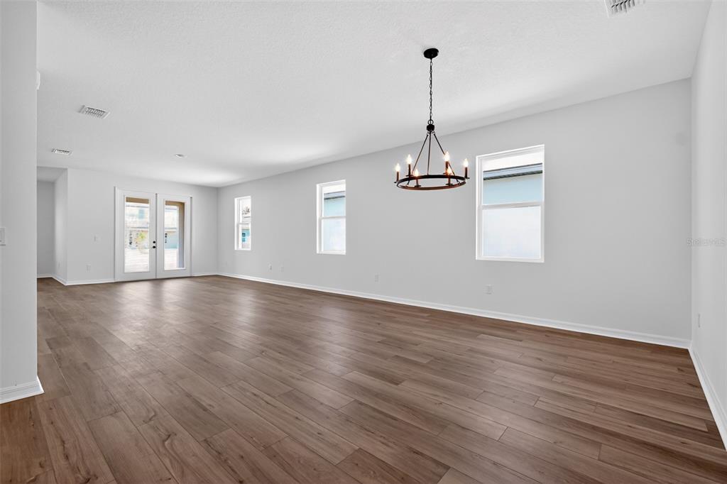 A spacious, empty room features light gray walls, wood-look flooring, and a rustic chandelier — 30130 EMERALD FOREST DRIVE, MOUNT DORA, FL