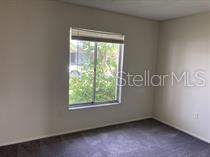 A bedroom with plain beige walls, gray carpeting, and a single window overlooking greenery — 11151 IRON BRIDGE ROAD, ORLANDO, FL