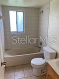 A bathroom features a tiled tub-shower combination, a white toilet, and light-colored floor tiles — 11151 IRON BRIDGE ROAD, ORLANDO, FL