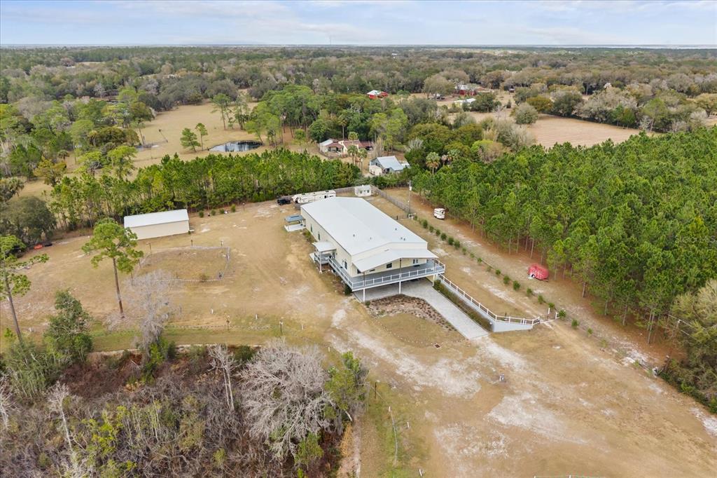 An aerial view shows a metal-roofed house on stilts surrounded by trees and open land — 455 BRIAR PATCH LANE, GENEVA, FL