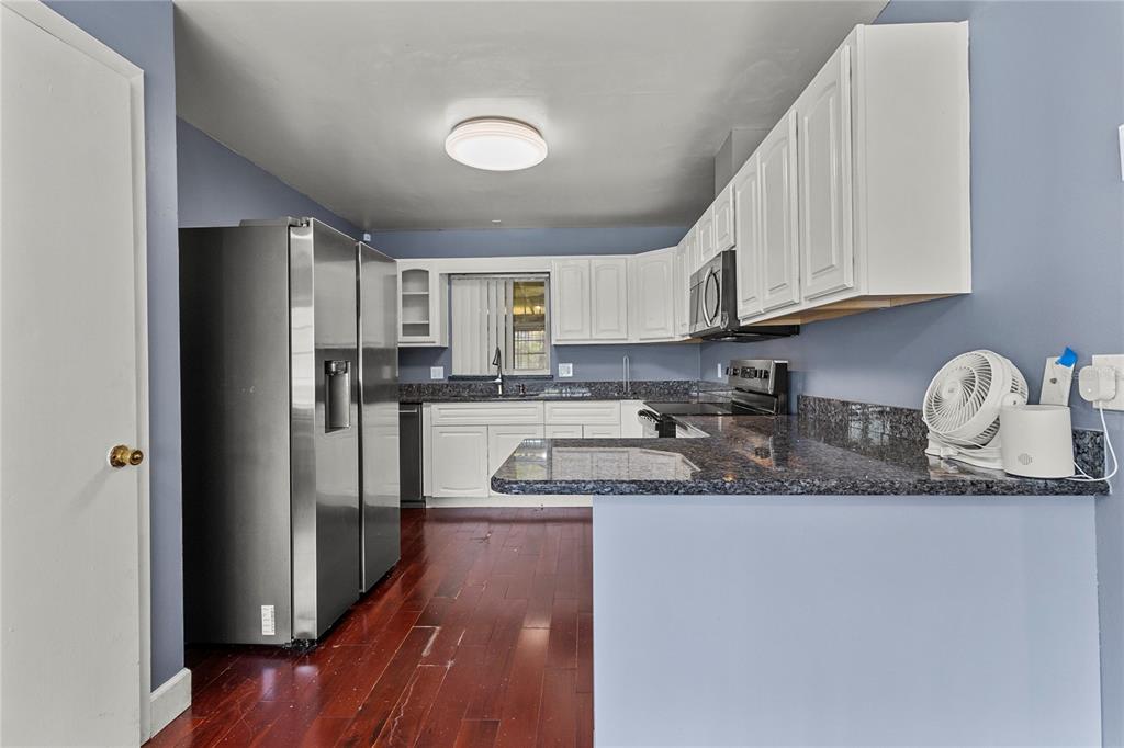 A living room with hardwood floors, a brown leather sofa, and an open kitchen area — 1700 NEEDLEWOOD LANE, ORLANDO, FL