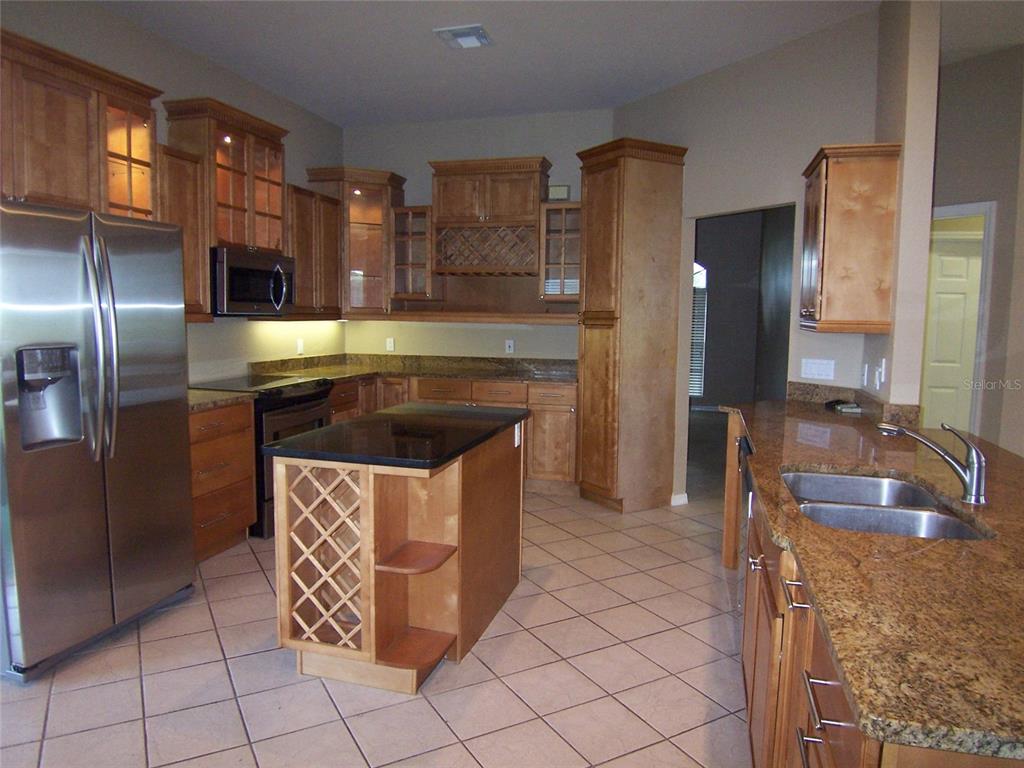 A kitchen features wood cabinets, granite countertops, a center island with wine storage, and stainless appliances — 5435 SUMMERLAND HILLS DRIVE, LAKELAND, FL