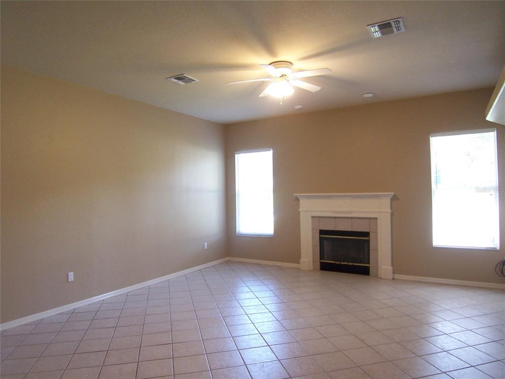 A living room features beige walls, tile flooring, a ceiling fan, and a white fireplace — 5435 SUMMERLAND HILLS DRIVE, LAKELAND, FL