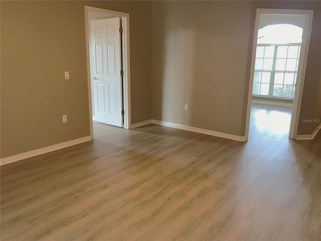 An empty room features light wood-look flooring, beige walls, a white door, and a large window — 5435 SUMMERLAND HILLS DRIVE, LAKELAND, FL