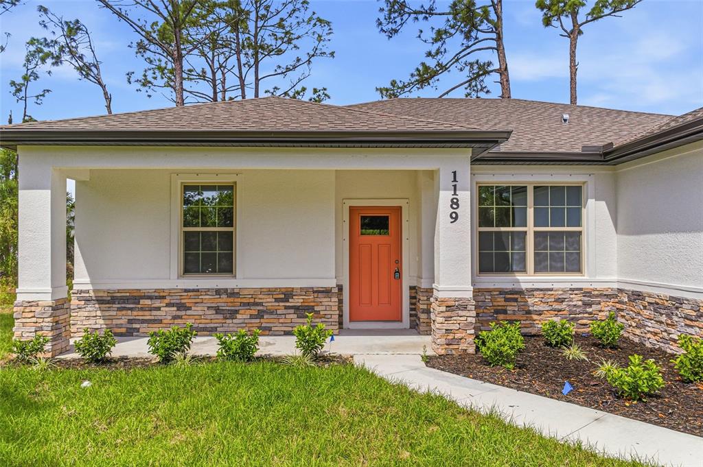 The exterior of a single-story house features a covered porch, stone siding, and an orange door — 3008 BREWSTER ROAD, NORTH PORT, FL