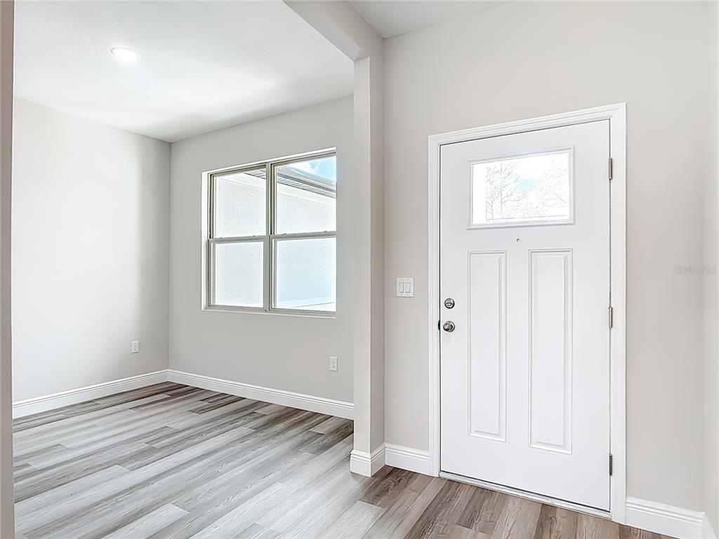 An entryway with light gray walls, wood-look flooring, and a white front door with glass — 3008 BREWSTER ROAD, NORTH PORT, FL