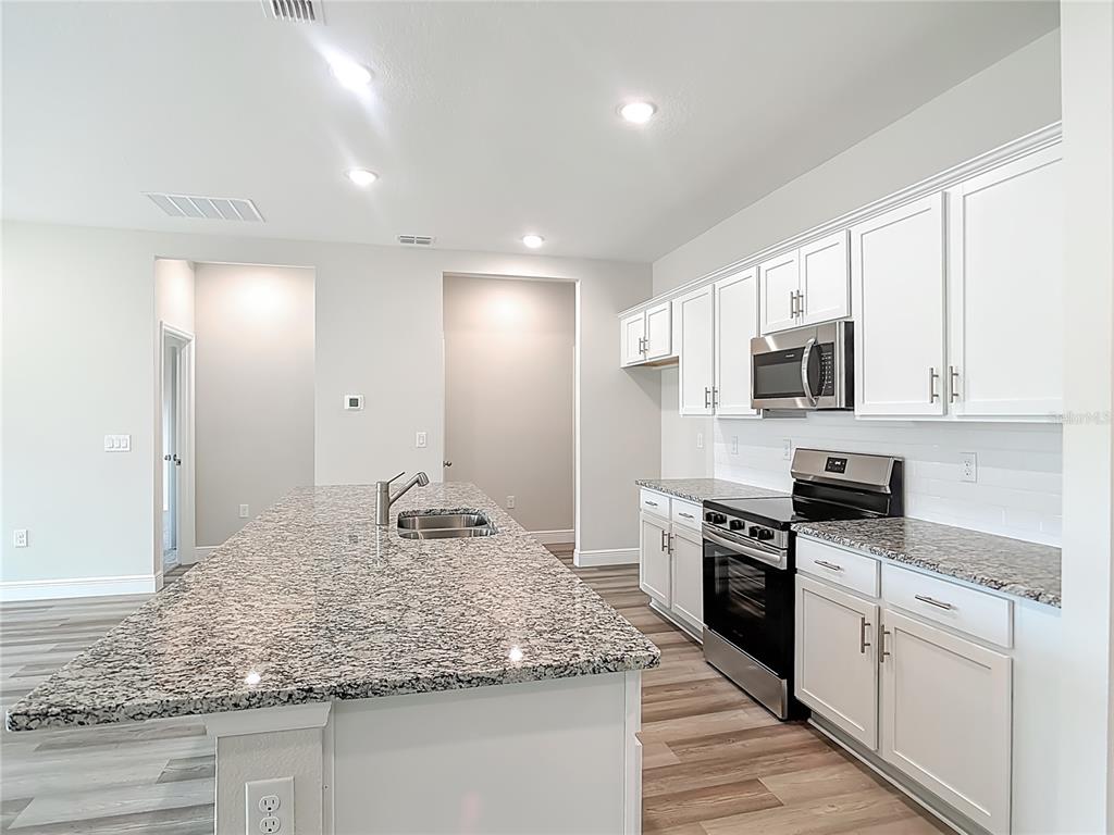 A kitchen features white cabinets, granite countertops, a large island, and stainless steel appliances — 3008 BREWSTER ROAD, NORTH PORT, FL