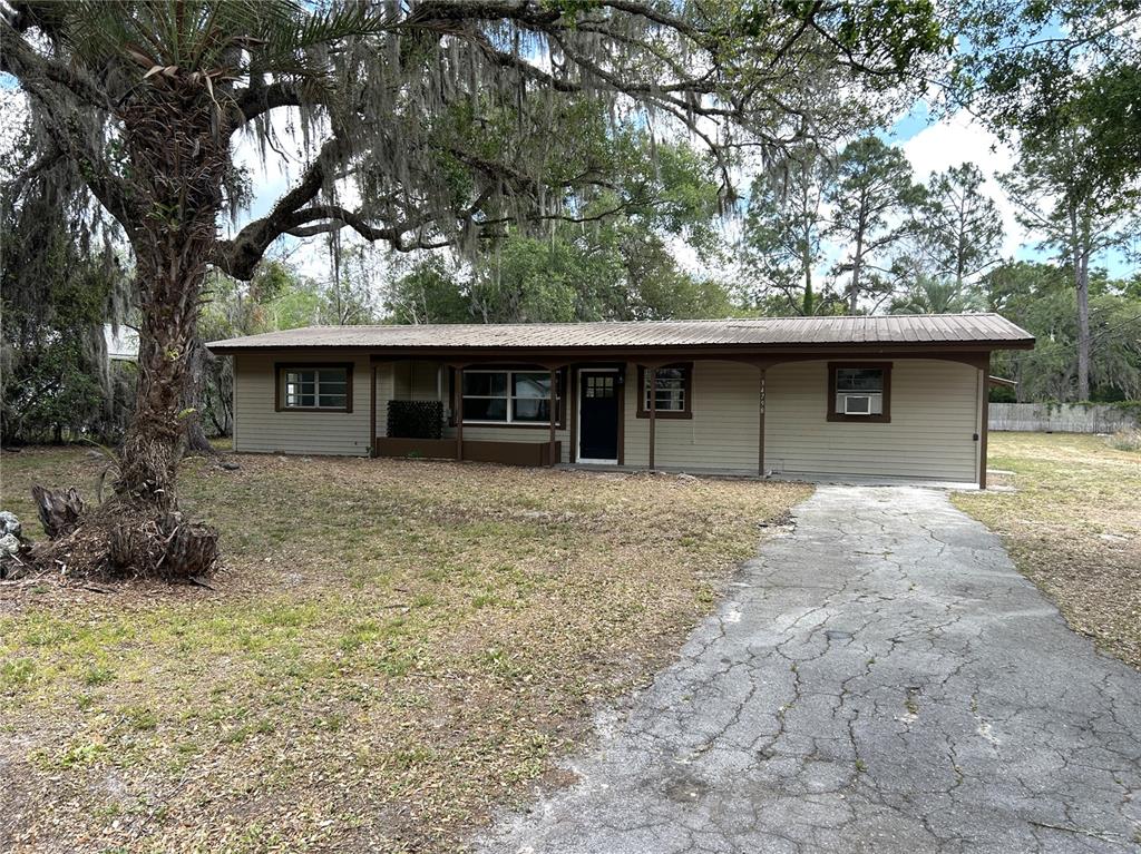 A single-story house with tan siding, a metal roof, and a covered front porch — 34798 EVERGREEN WAY, DADE CITY, FL