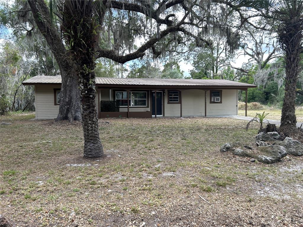 A single-story house with tan siding and a covered porch sits among large trees — 34798 EVERGREEN WAY, DADE CITY, FL
