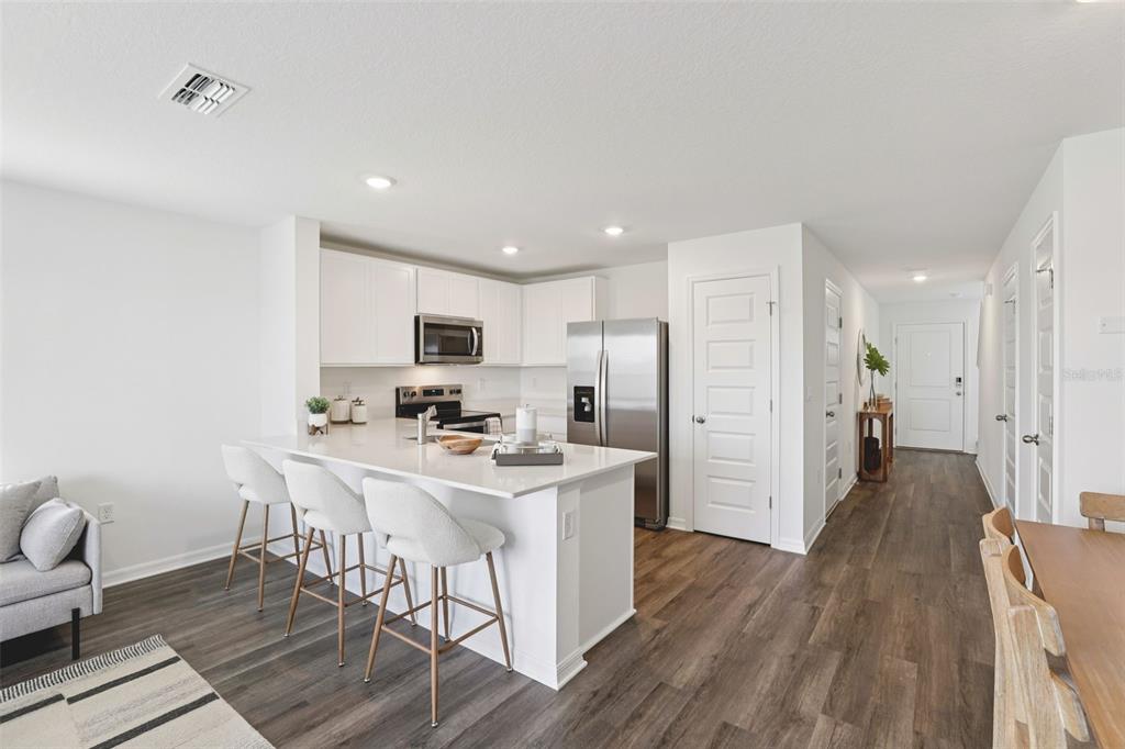 A modern kitchen features white cabinetry, stainless steel appliances, and a quartz-topped island with seating — 4706 TONY STREET, LAKE WALES, FL