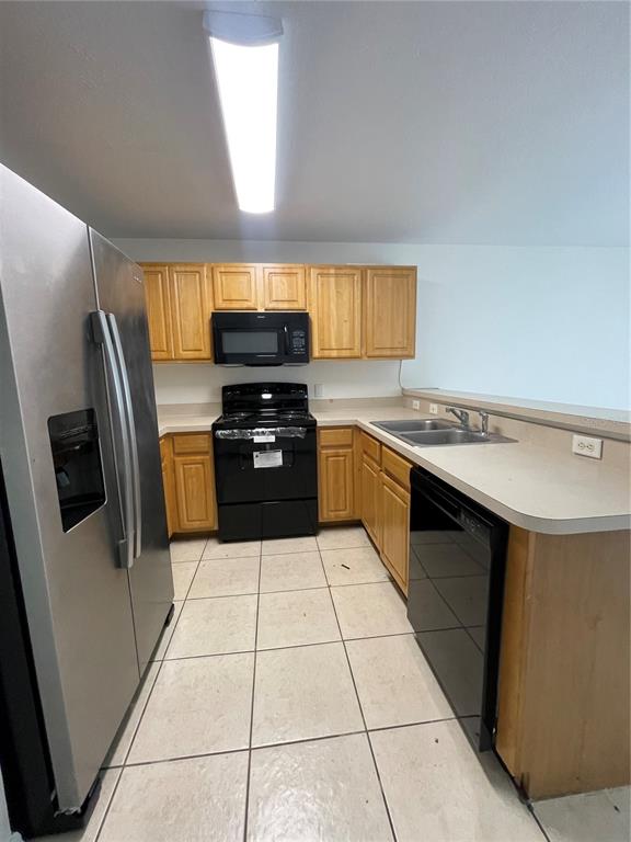 A kitchen features light wood cabinets, black appliances, a stainless steel refrigerator, and tiled flooring — 342 CERVANTES DRIVE, KISSIMMEE, FL