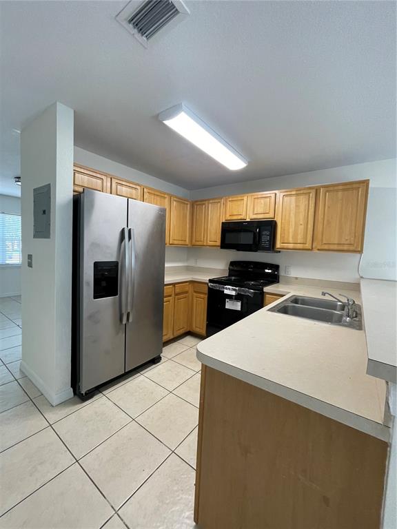 A kitchen features light wood cabinets, stainless steel appliances, and beige countertops over tiled floors — 342 CERVANTES DRIVE, KISSIMMEE, FL
