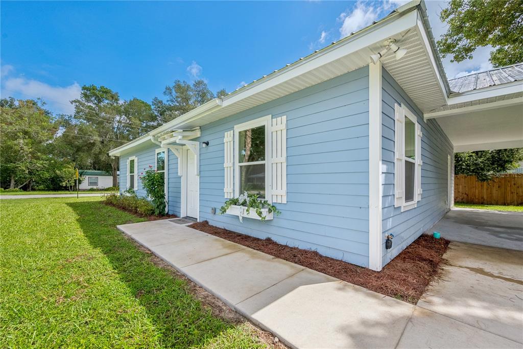 A light blue house with white trim, shutters, and a concrete walkway leading to a carport — 506 NE FOURTH STREET, TRENTON, FL