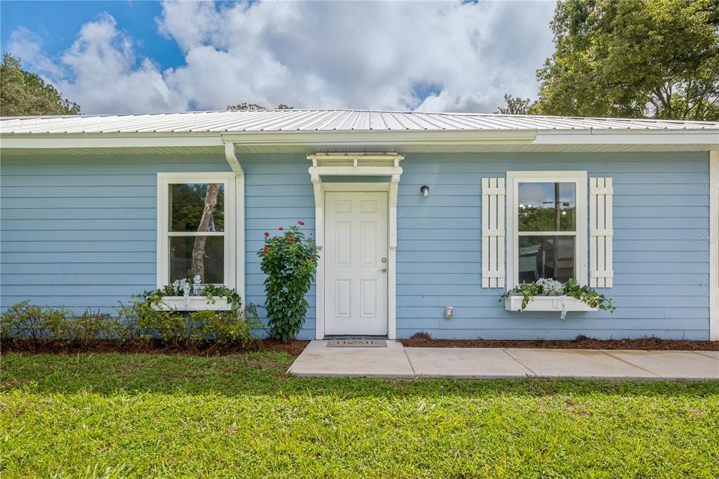 A light blue house exterior features a white front door, two windows with shutters, and planters — 506 NE FOURTH STREET, TRENTON, FL