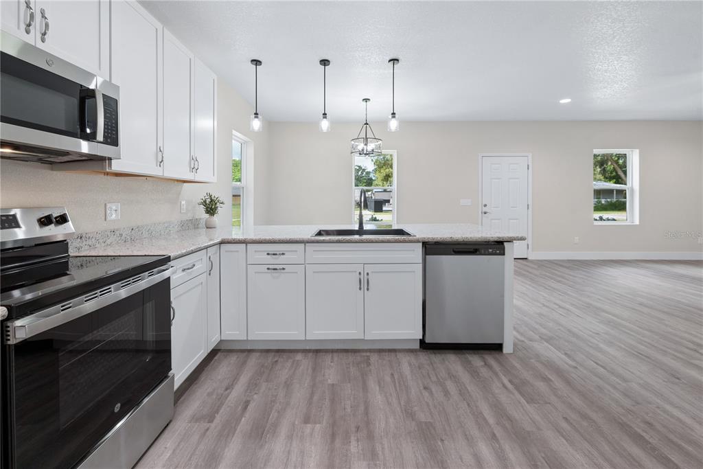 A kitchen with white cabinets, stainless steel appliances, granite countertops, and light wood-look flooring — 506 NE FOURTH STREET, TRENTON, FL