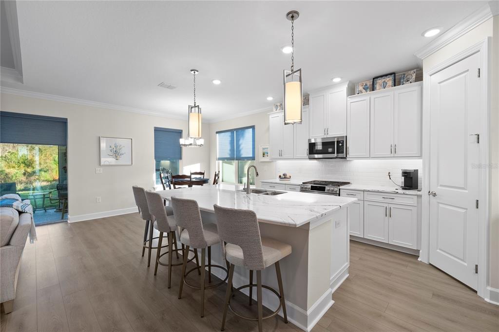 A modern kitchen features white cabinetry, a marble-topped island with bar stools, and wood flooring — 4618 ISONZO WAY, WESLEY CHAPEL, FL