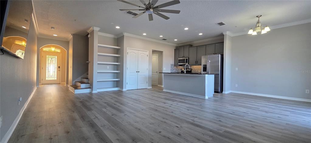 An open-concept living area features light wood-look flooring, a kitchen with gray cabinets, and stairs — 760 WALKERS GROVE LANE, WINTER GARDEN, FL