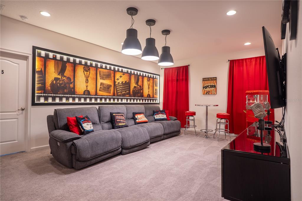 A home theater room features a gray sectional sofa, film strip wall art, and red curtains — 2610 TRANQUILITY WAY, KISSIMMEE, FL