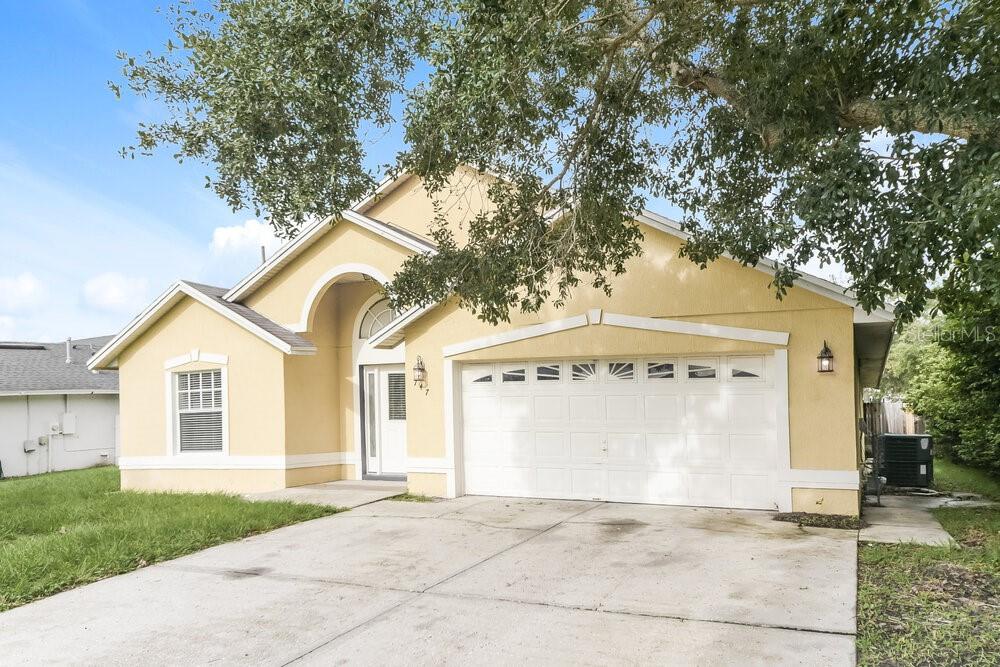 A single-story yellow stucco house features a two-car garage and a large tree in front — 747 CITRUS COVE DRIVE, WINTER GARDEN, FL