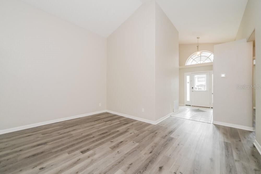 An empty room with light-colored walls and wood-look flooring leads to a tiled entryway — 747 CITRUS COVE DRIVE, WINTER GARDEN, FL